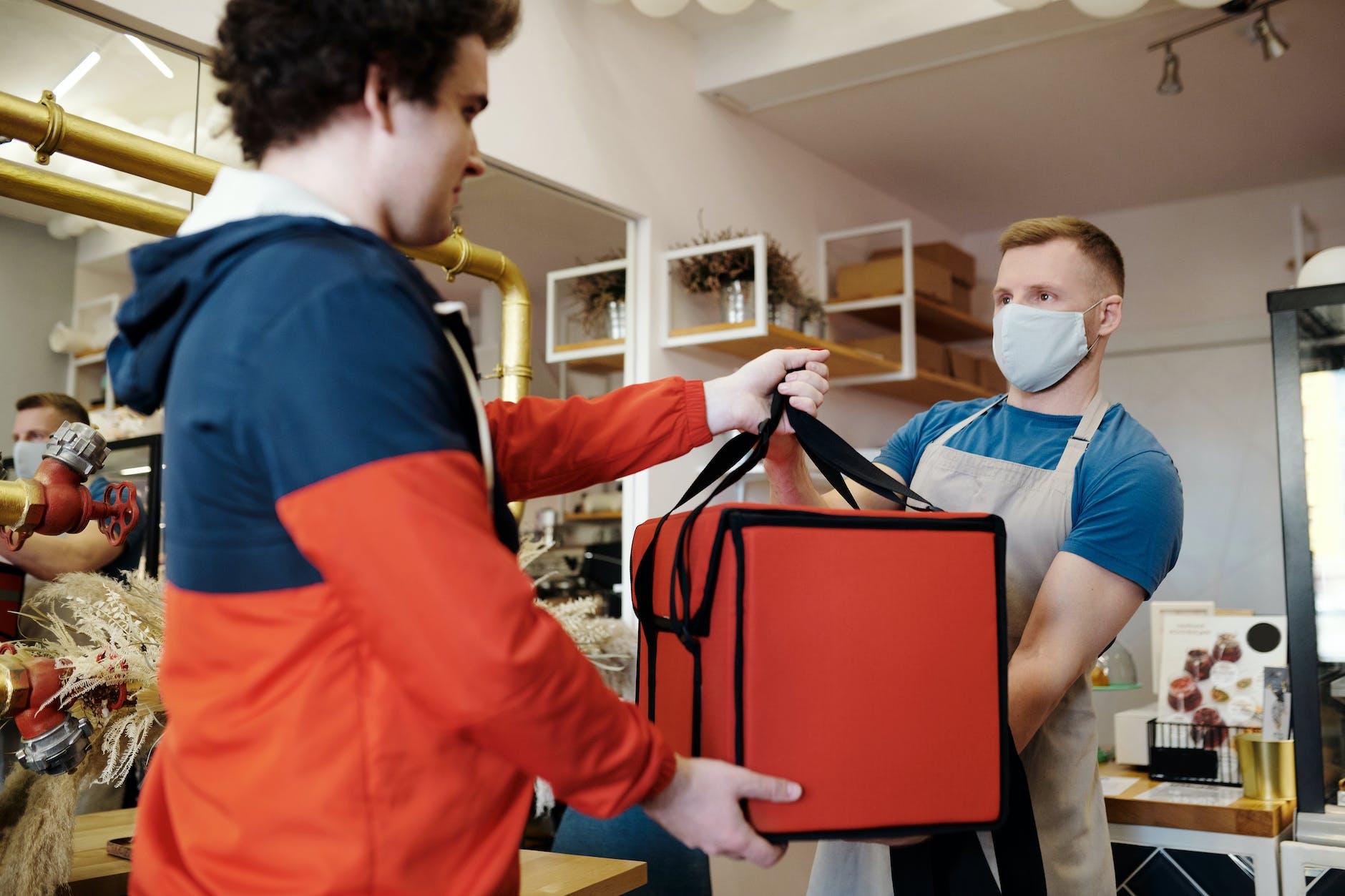 man in a face mask handing over a thermal bag to another man