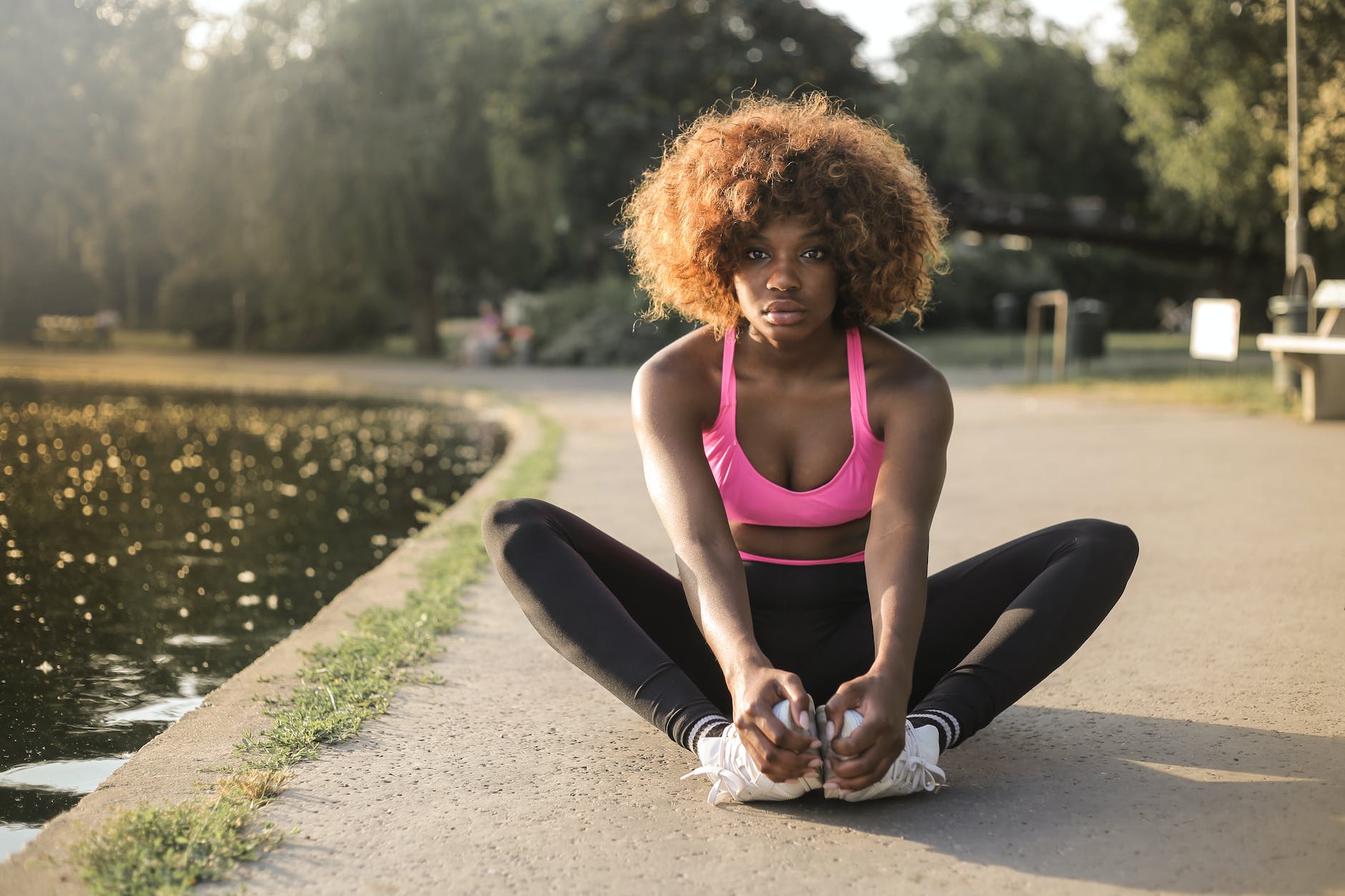 woman in pink tank top and black leggings sitting on gray concrete pathway