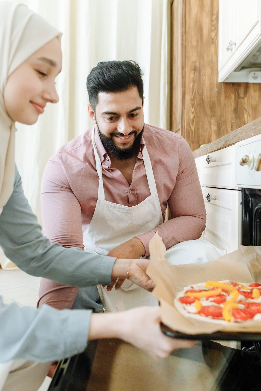 a bearded man looking at the woman baking pizza