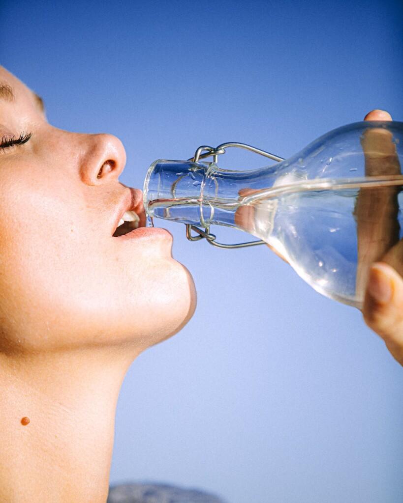 woman drinking water from glass bottle