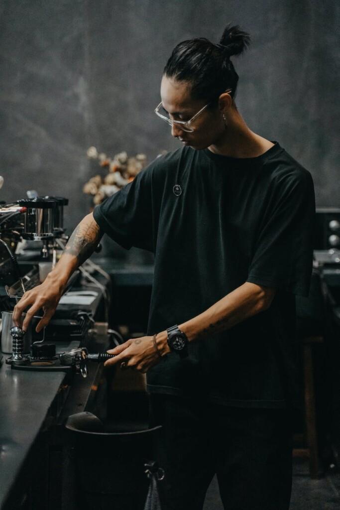 a man in black shirt making coffee while holding a portafilter