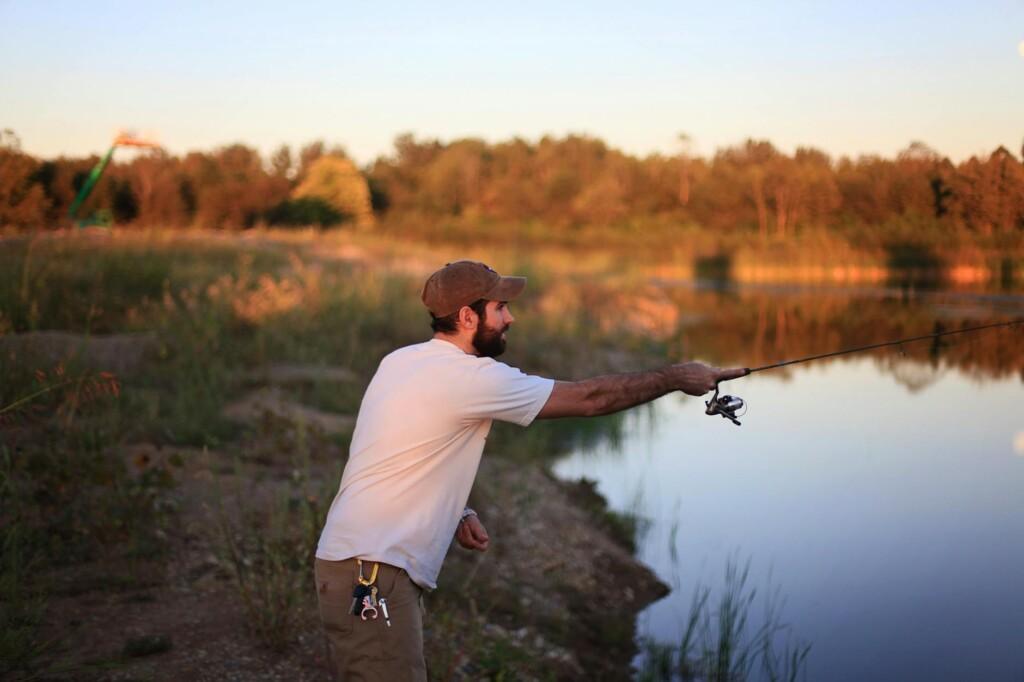 man fishing on pond near grass field