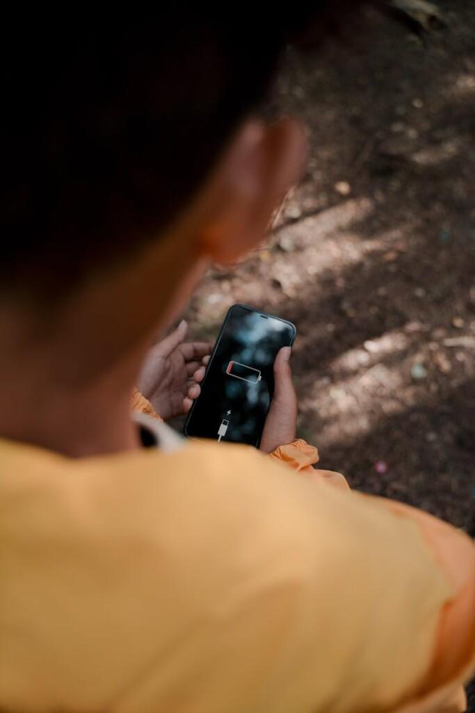 Teenager with low battery smartphone in forest reflects solitude and disconnect.