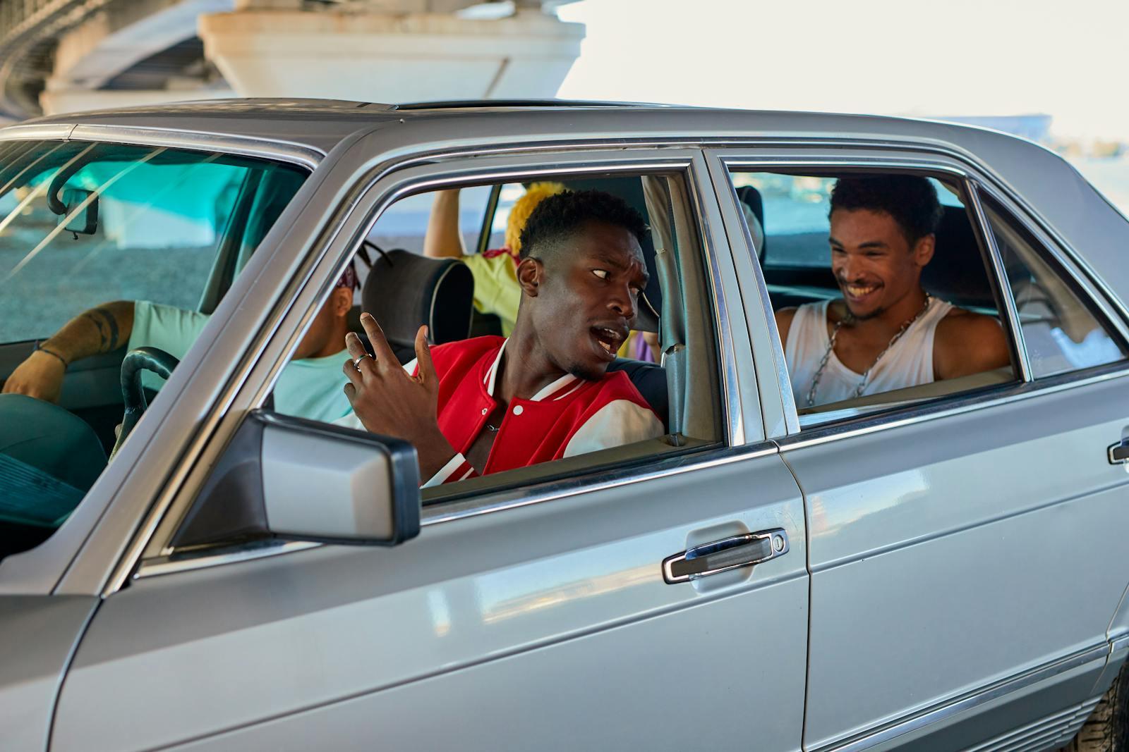 A group of young adults enjoying a lively conversation in a classic car outdoors.