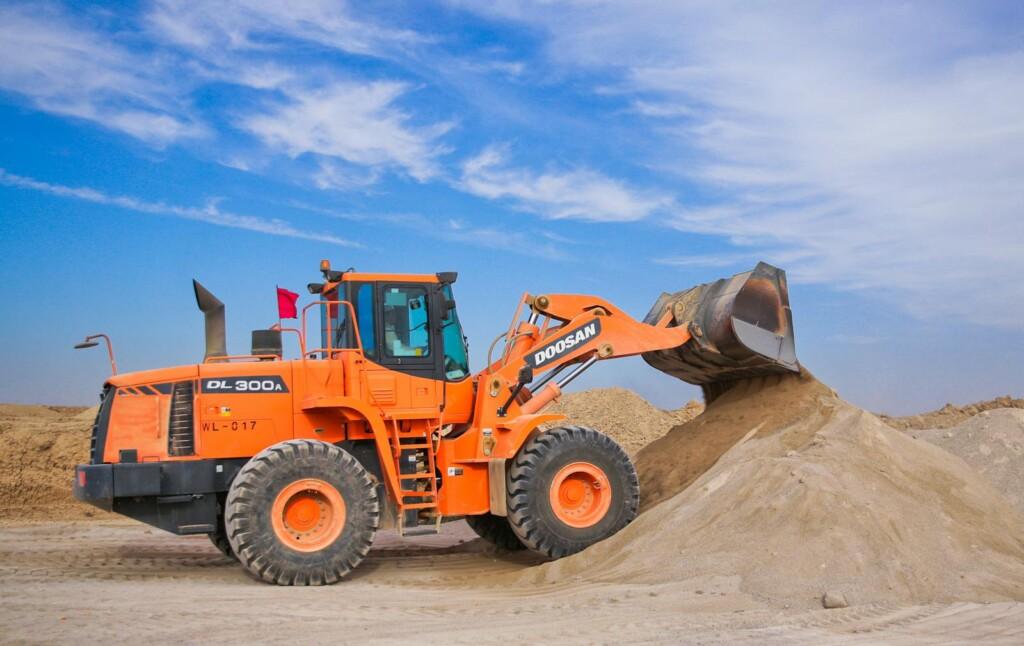 An orange bulldozer at work, moving sand under a clear blue sky on a construction site.