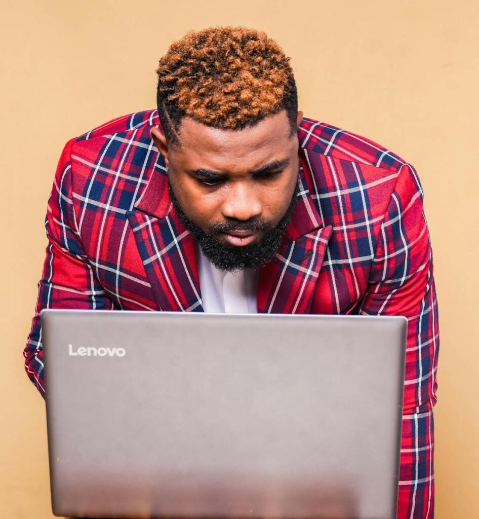 Man in plaid jacket intensely focuses on work using a laptop, indoors.