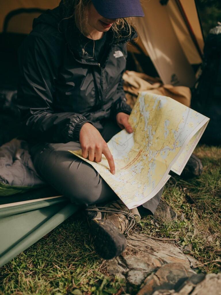 A woman sits in a tent studying a map during a camping trip in the wilderness.