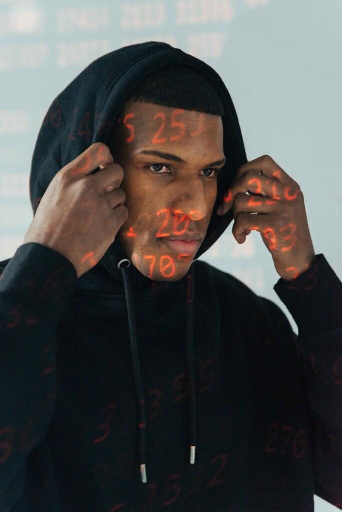 Portrait of a cybersecurity expert wearing a hoodie with projected digital data and numbers.