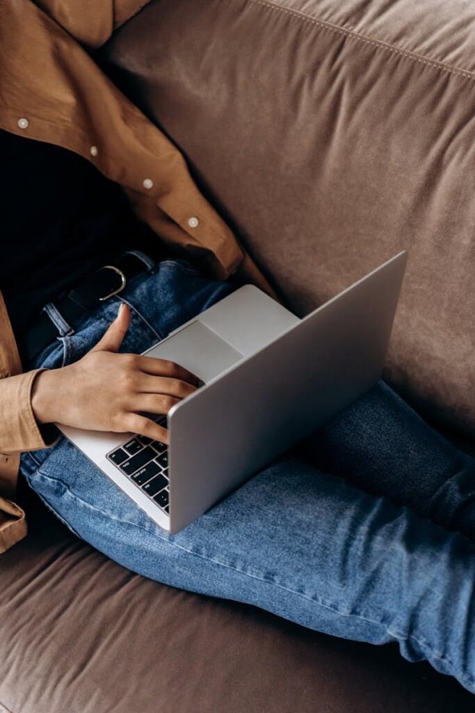 Close-up of a person using a laptop while lounging on a sofa, embodying a relaxed work-from-home vibe.