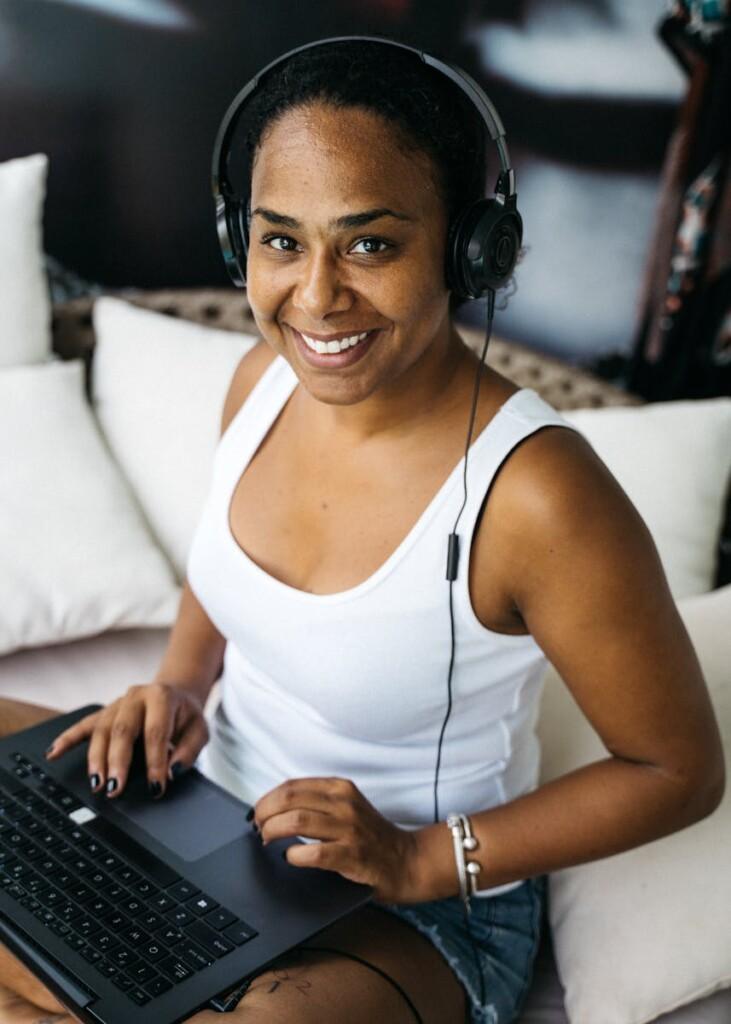 A woman with headphones enjoys remote work on a laptop in a cozy setting.