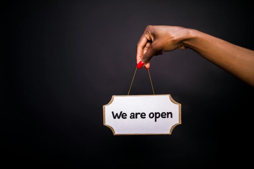 Close-up of a hand holding a 'We are open' sign against a black background.