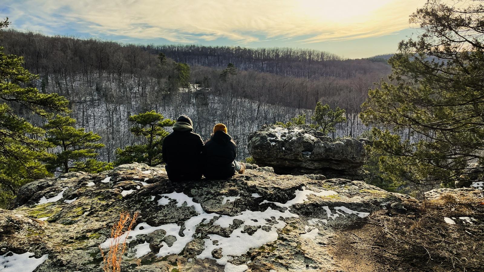 two people sitting on top of a rocky cliff