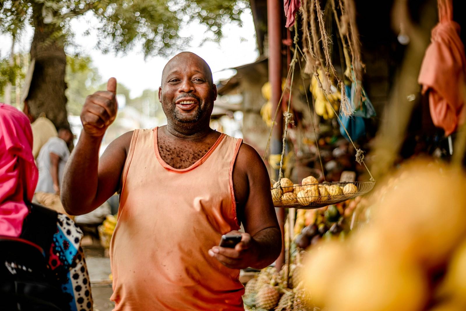 a man standing in front of a fruit stand giving a thumbs up