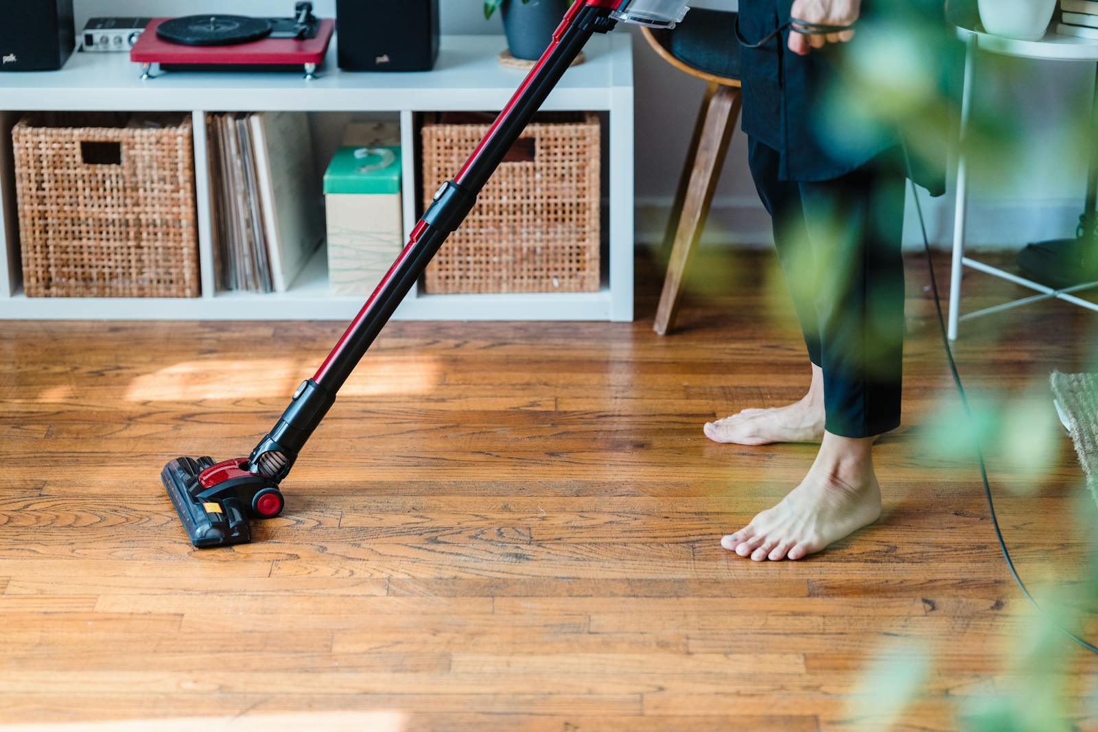 A person vacuuming wooden flooring in a cozy room, emphasizing clean living space.