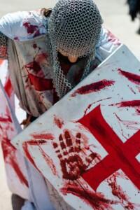 A man dressed as a medieval knight with a blood-splattered shield and armor in cosplay.