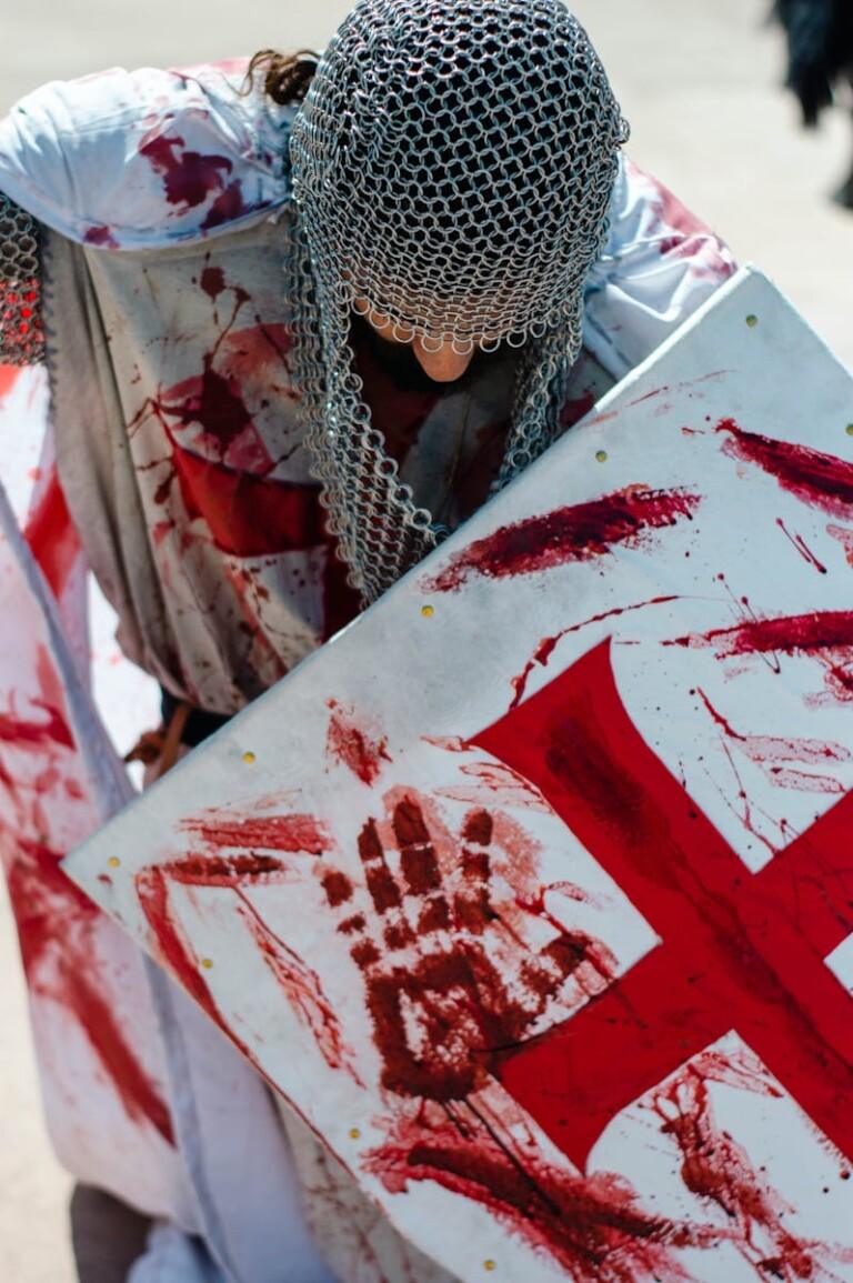 A man dressed as a medieval knight with a blood-splattered shield and armor in cosplay.
